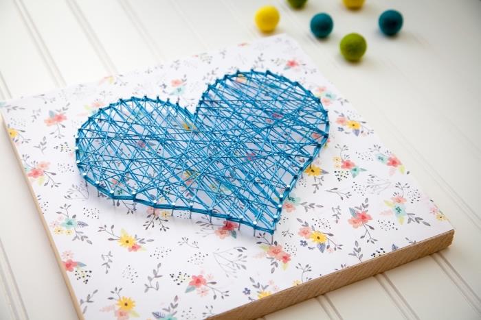 vacker DIY -skapelse på en rektangulär träskiva täckt med färgglatt scrapbookingpapper och blå tråd