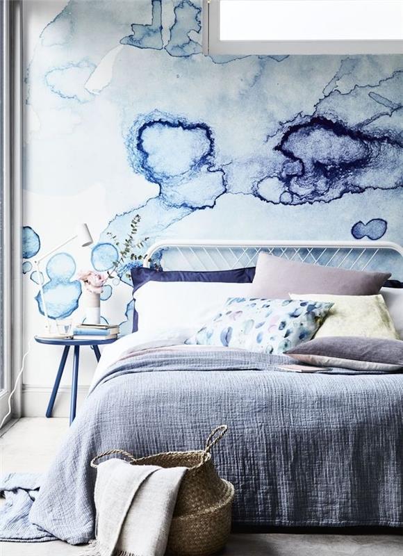 model tapety do spálne, modré škvrny na bielom pozadí, akvarelový efekt, sivá posteľná bielizeň, vankúše, biela, modrá, žltá a ružová, prikrývkový úložný kôš