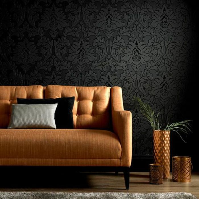 fiberduk tapet i svart med arabeskmönster, med 3D-effekt, soffa i beige, kruka med grön växt och vas i bronsfärg med triangulära mönster i relief