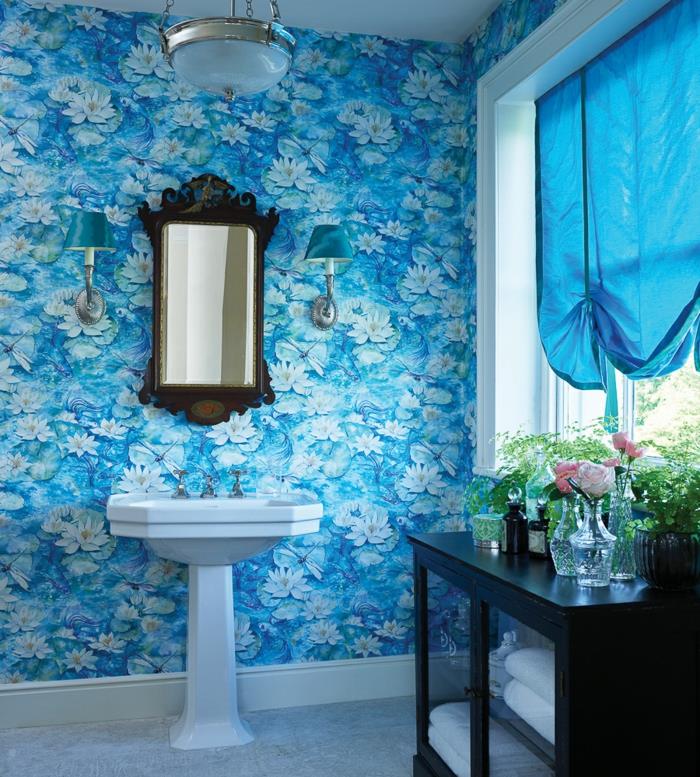 trompe l'oeil tapet med stora blå och vita blommor, badrum i romantisk stil, svart skåp, halvtransparenta blå draperade gardiner, mörkbrun backspegel i barockstil, stort vitt handfat, armatur i vintage stil, två vägglampor med blå lampskärmar med silverfärgade metallelement