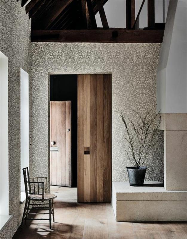 trompe l'oeil tapet, stor vit eldstad i slottsstil, ljus parkett, svart stol, utrymme under takfoten, med massiva balkar i brun färg, stor svart kruka med ett litet träd