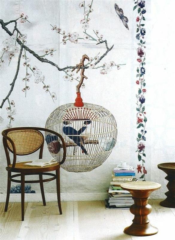 trompe l'oeil tapet med stort fågelbur motiv uppe på ett träd, blommande körsbärsträd med känsliga rosa blommor, sovrum med stol i asiatisk stil, två pallar i ljust och mörkt trä, parkett i vitt och beige