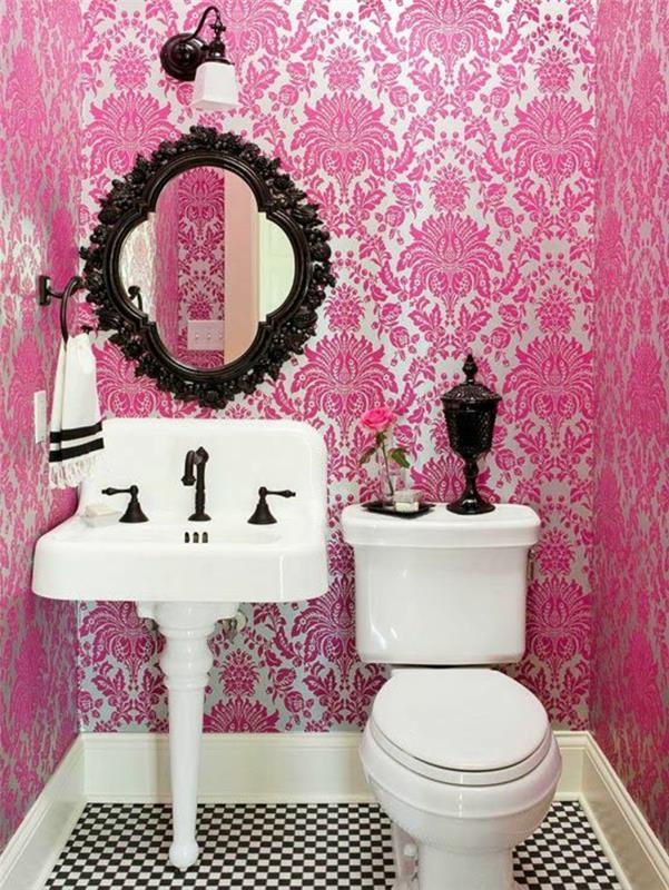 trompe l'oeil tapet i rosa och vitt, med arabeskmönster, badrum med barockspegel i svart trä, svart metallvägglampa och vit lampskärm, vit handfat i vintagestil, svartvitt kakel med dekorativa mönster schackbräda