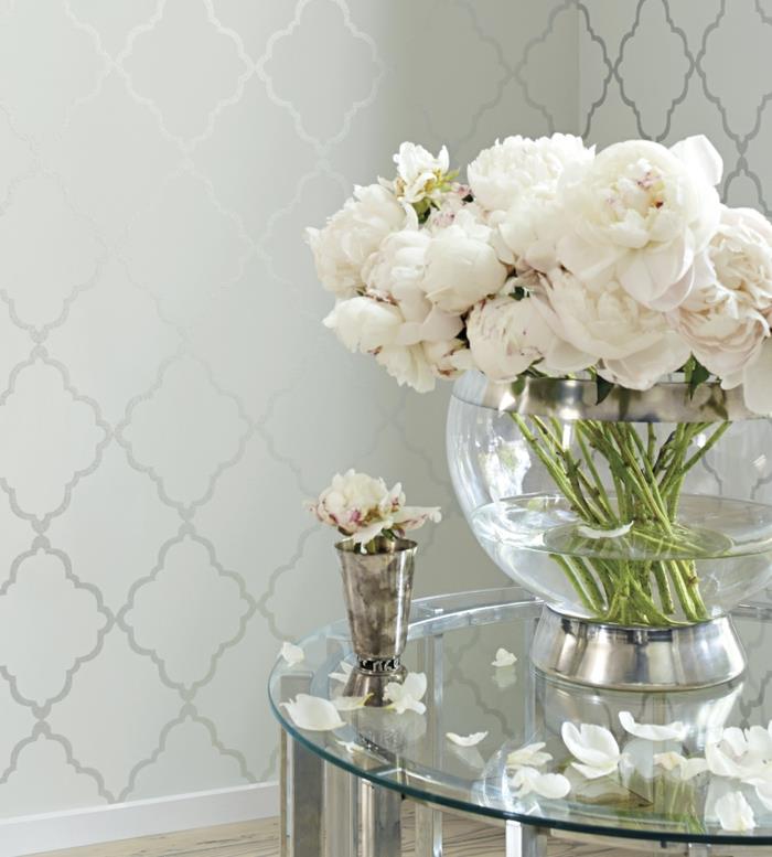 trompe l'oeil tapet liberty tapet i satengrått, stor skål i transparent vitt glas med vita rosor, litet soffbord i vitt glas i rund form, med silverfärgade metallben, grå parkett