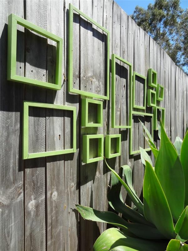 vonkajšia stena pokrytá starými rámami na obrazy premaľovanými na zelený rezeda, sivý drevený záhradný plot so starým efektom, veľká exotická zelená rastlina
