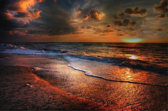 solnedgångshimmel i röda och orange toner, lugna vågor, grumlig himmel, overkligt ljus över havet