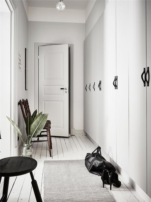 Hall i skandinavisk stil med vita väggar med inslag av svart på möblerna, hallskåp med inbyggd förvaring