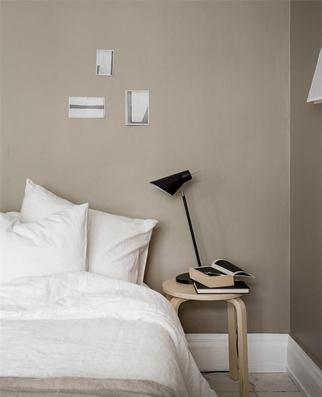 لون رمادي فاتح على جدران غرفة النوم باللونين الرمادي والأبيض ، وبياضات أسرّة بيضاء ، وطاولة خشبية فاتحة سوداء ، ومصباح سرير أسود مصمم