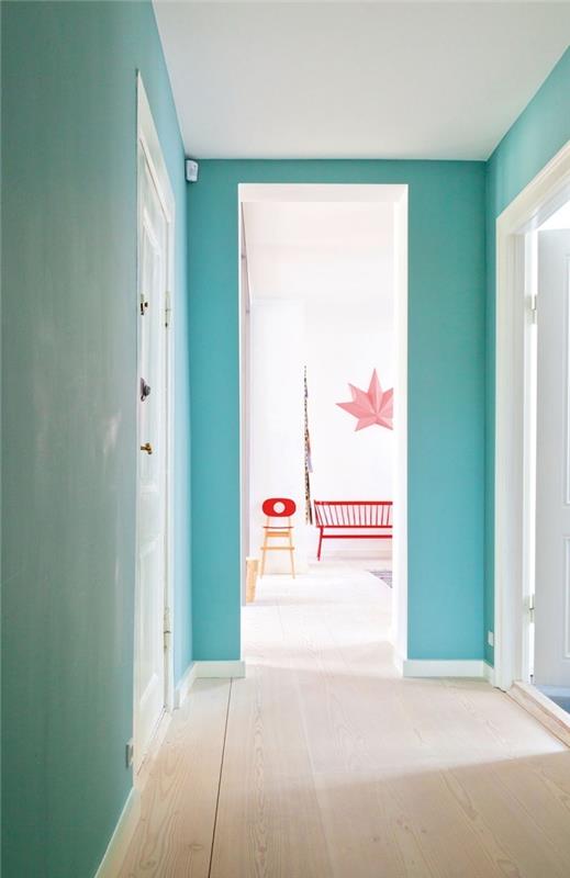 väggarnas turkosblå harmonierar perfekt med de vita dörrarna och den ljusa parketten för att skapa en modern och lugnande atmosfär i korridoren
