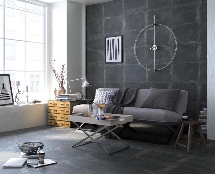 industriellt vardagsrum med mörkgrå vägg och stort fönster, grå soffa täckt med kuddar och dekorativ pläd i grå nyanser