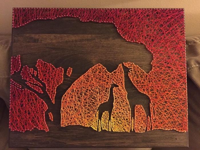 vacker skapelse på temat Afrika med en mörk träskiva och ett solnedgånglandskap och giraffer i sytråd