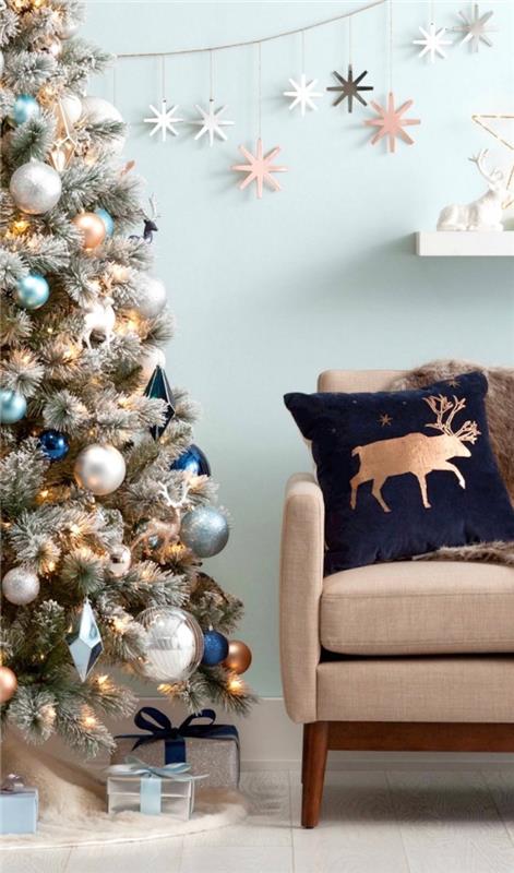 modern inredning i ett vardagsrum med pastellblå väggar möblerade med tyg och mörka trämöbler, julgransdekoration med metalliska prydnader
