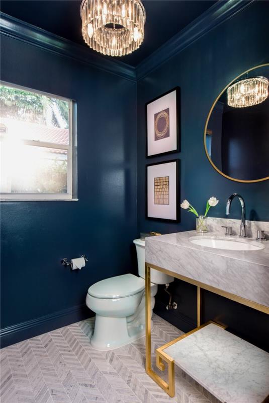 kryštálové stropné svetlo na toalete, svetlošedé umývadlo, modrá farba na stenu, toaleta v modrobielom prevedení, oválne zrkadlo v zlatom ráme