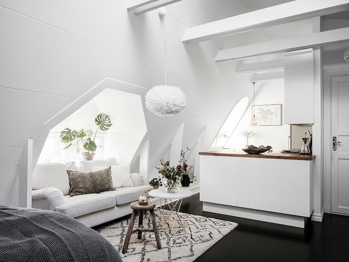 utrymme under sluttningen med vita väggar med central ö med bänkskiva i trä, svart och vit matta, vita synliga balkar, original vit taklampa