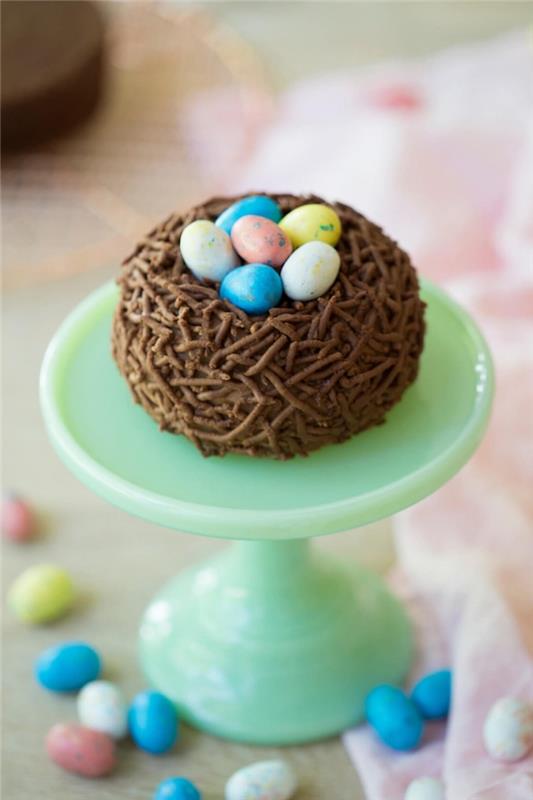 choklad påskbo cupcake toppad med chokladägg på pastellgrönt tårtställ, klassisk påsktårta
