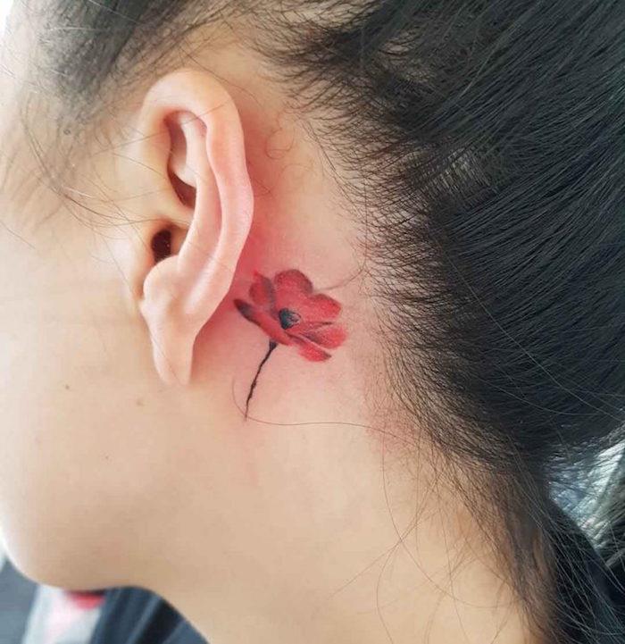 liten vallmotatuering bakom kvinnans röda öra, minimalistisk vallmo för att tatueras