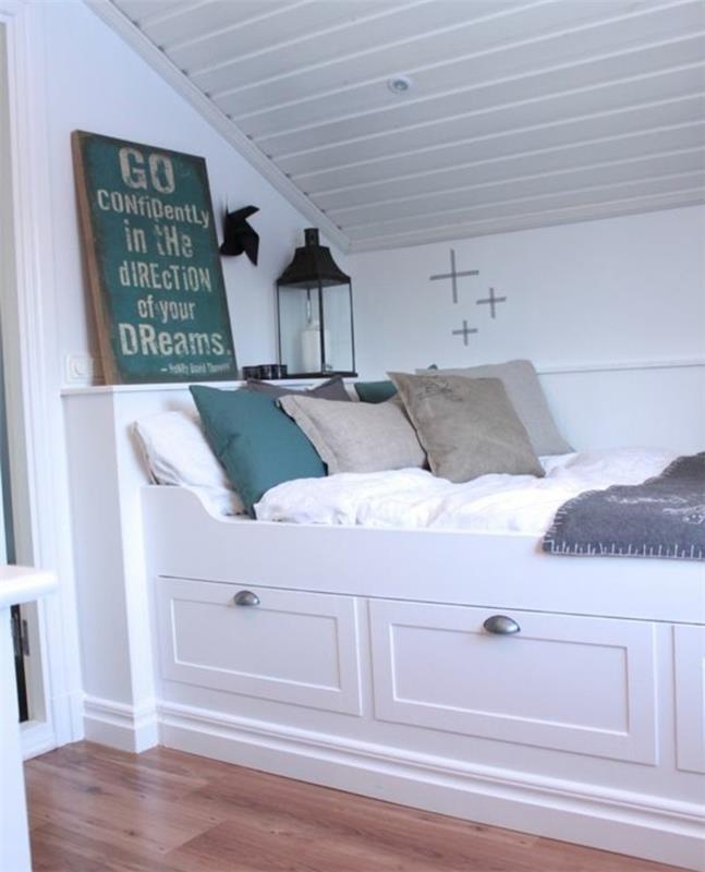 litet vindsovrum, vit säng med förvaring, vita sängkläder, grå och gröna kuddar, ljus parkett, vit väggfärg, vindsovrum