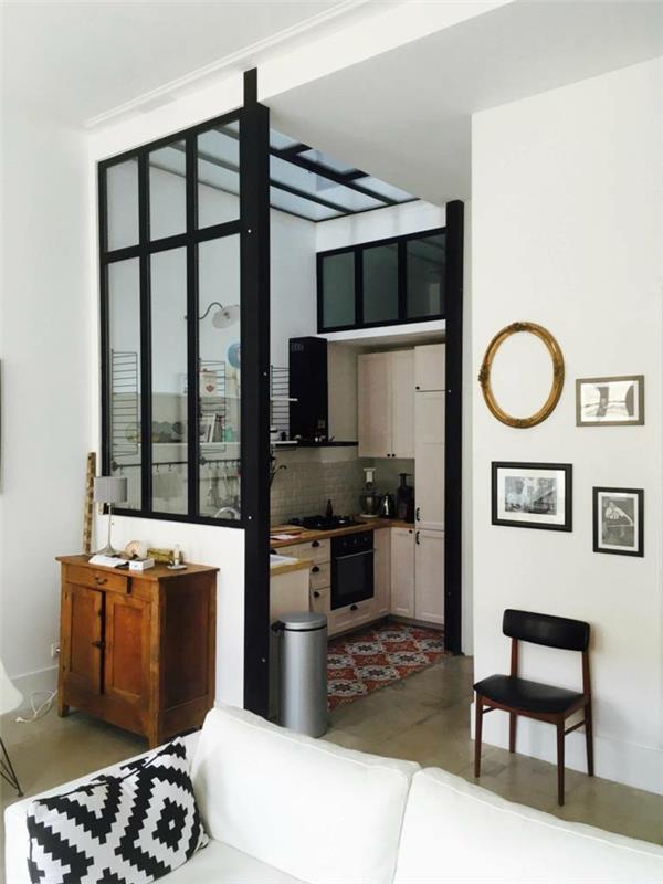 malá kuchyňa v tvare L s priečkou z čierneho skla v umeleckom ateliéri, príborník z rustikálneho dreva, veľká biela pohovka, geometrický vankúš