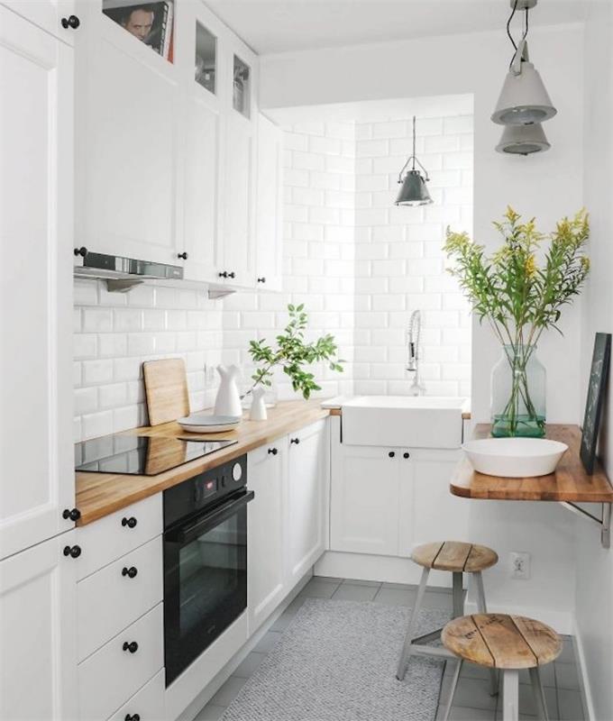 نموذج مطبخ أبيض مجهز بخزانة عالية بيضاء وخزانة منخفضة وسطح عمل خشبي وسبلاش باك وجدار من البلاط الأبيض