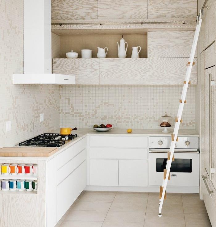 مطبخ صغير أبيض على شكل حرف L مع خزانة قاعدة بيضاء وخزانة علوية خشبية ، مكنسة كهربائية بيضاء ، بلاط بيج ، مطبخ مغطى بالبلاط الأبيض والبيج