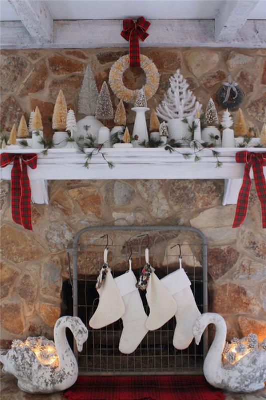 زينة عيد الميلاد على مدفأة حجرية مع رف خشبي أبيض وجوارب وشموع وأشجار صغيرة