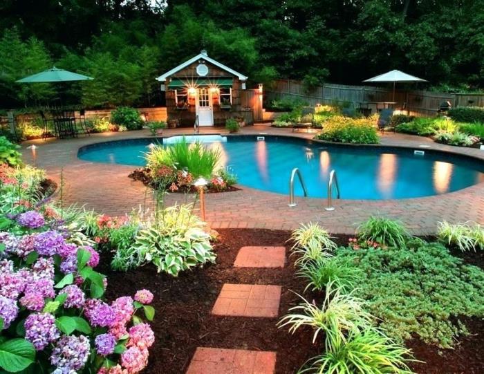 حمام سباحة بأشكال منحنية وسرير زهور وأزهار أرجوانية ومساحة كبيرة ذات مناظر طبيعية وحديقة في الغابة