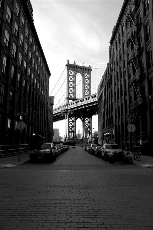 vy över en del av New York -bron mellan höga byggnader, svartvitt stadsbild från ett ursprungligt perspektiv