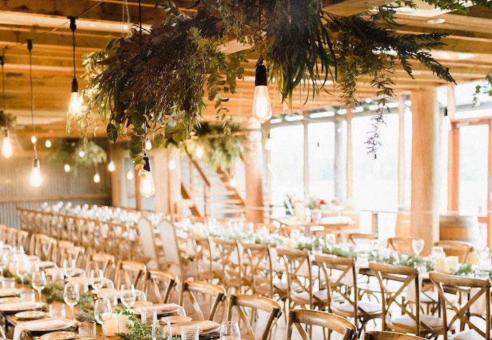 priemyselné zavesenie žiaroviek a dekorácia kvetinového lístia nad dreveným stolom a stoličkami a malá dekorácia zeleného lístia
