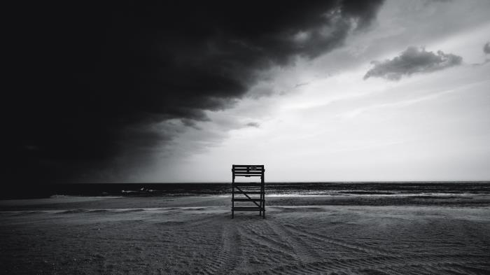 svartvitt havslandskap på en öde strand med en ensam livräddarstation och en stormig himmel halvtäckt av moln