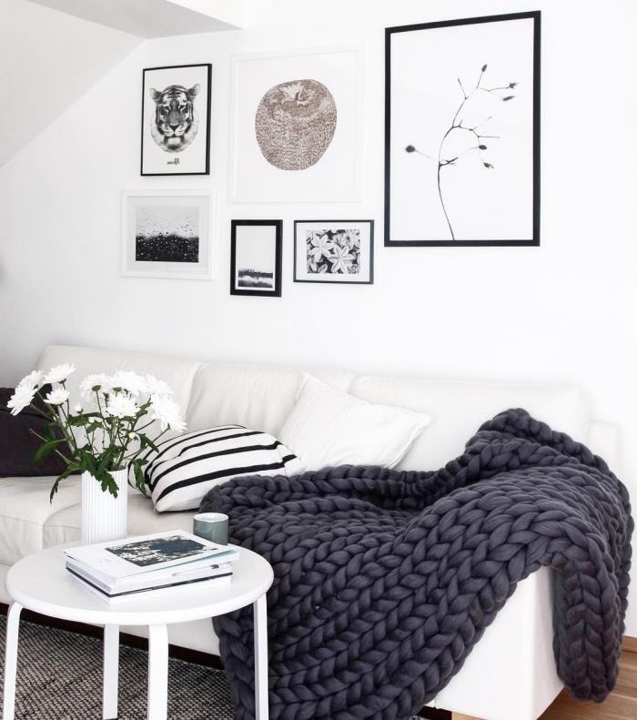 litet svartvitt vardagsrum i en ren och minimalistisk skandinavisk stil med en traditionell cocooning -anda för de nordliga länderna, kokong och personlig dekoration med ett monokromt vägggalleri och en vit soffa med en stor grå meshpläd