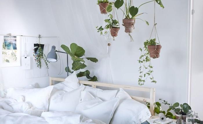nápad na výzdobu bielej spálne s kvetináčmi visiacimi nad drevenou posteľou s bielou posteľnou bielizňou, bytová rastlina