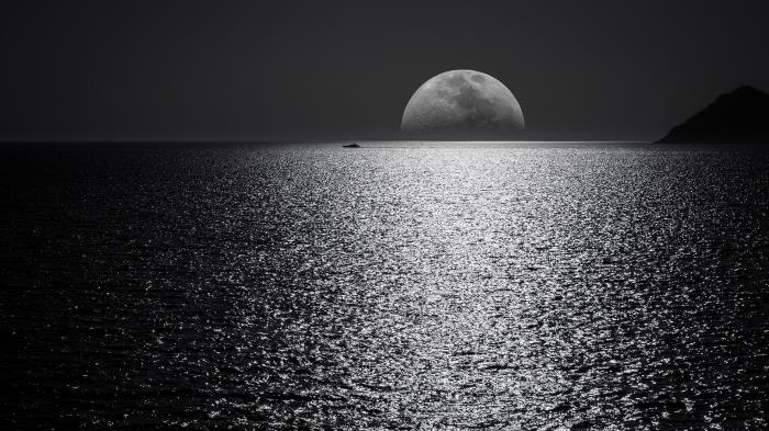 vackert panorama svartvitt foto av fullmånen som dyker upp under horisonten och dess reflektioner över det lugna havet