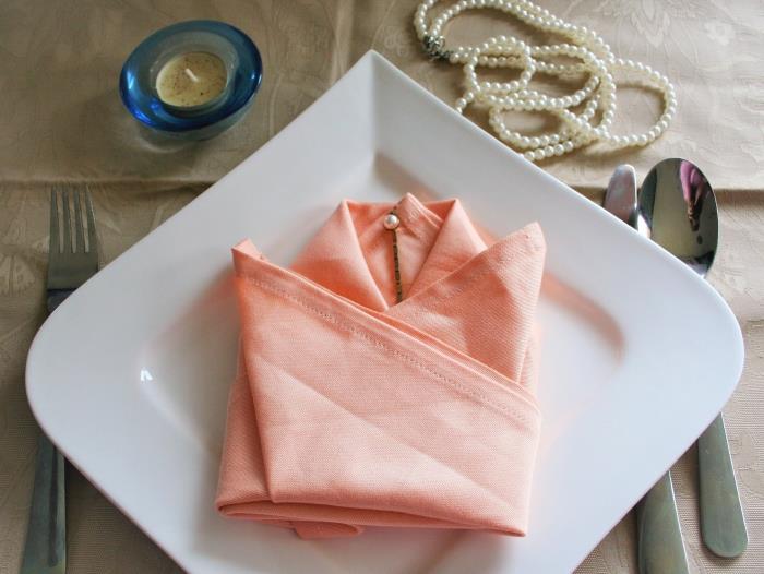 elegant festlig bordsdekoration med en korallfärgad servett vikt till en tulpan, blommformad påskservettfällningsidé