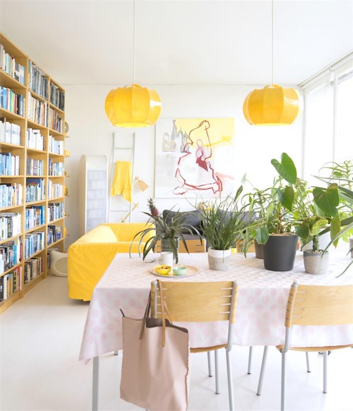 biela výzdoba obývačky so žltými a zelenými akcentmi, kvetináče naaranžované na stole za jasličkami, drevená knižnica, biele steny