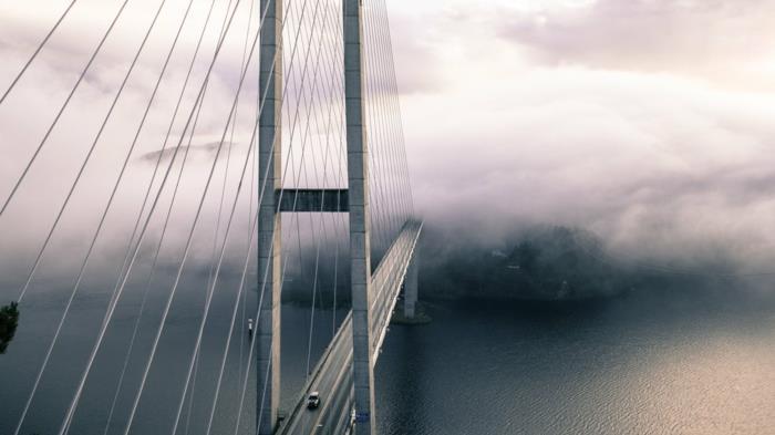 en bild av en bro som försvunnit i dimman, effekten av ett mystiskt paradisiskt landskap, bilar som passerar bron, vatten något upprörd av en bris