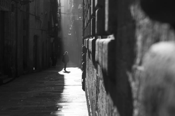 svartvitt fotografi av gatumannen som går ner i en smal gränd och ljuset faller på en del av trottoaren