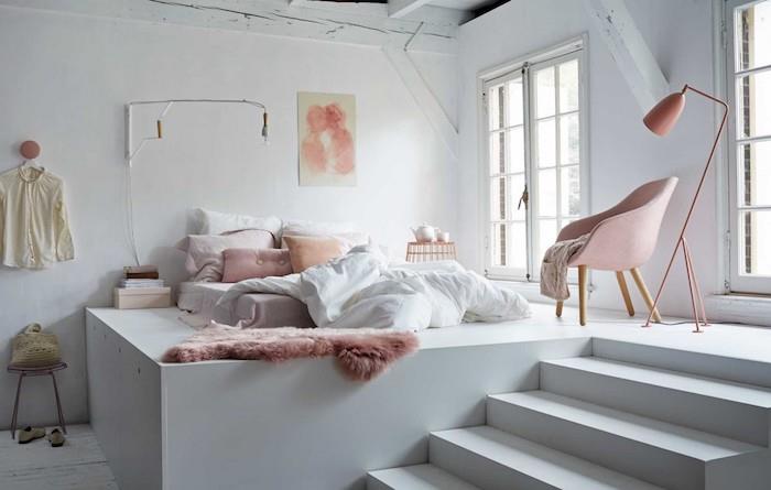 cocooning madrass på vit plattform, med kuddar och rosa pläd, vita väggar, rosa fåtölj, hygge atmosfär, romantisk studio sovrum inredning