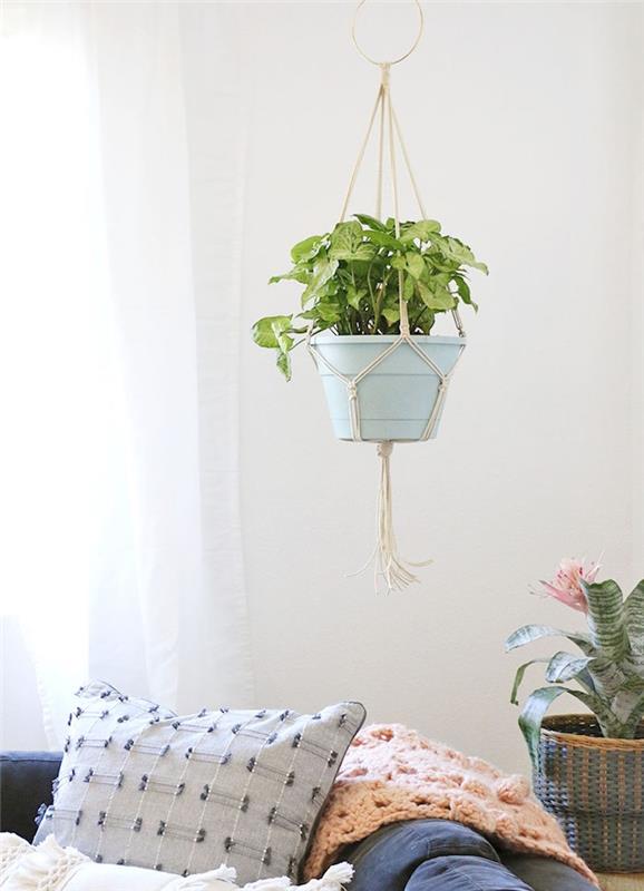 závesný kvetináč macrame a aechmea v kvetináči, dekorácia obývačky s bielymi stenami a modrou sedačkou zdobenou vankúšmi a ružovým plédom