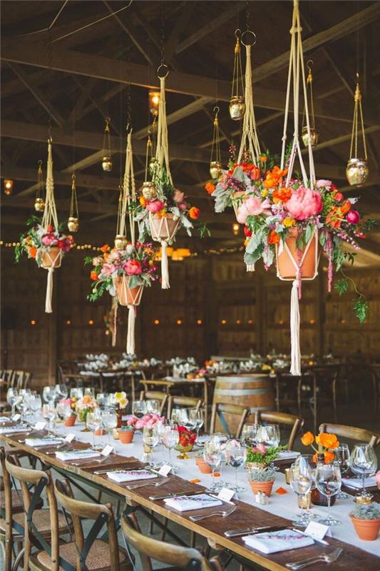závesné kvetináče macrame s farebnými kvetmi nad dreveným stolom a stoličkami, biely behúň na stôl, malé kvetináče, nápad na rustikálny elegantný svadobný dekor