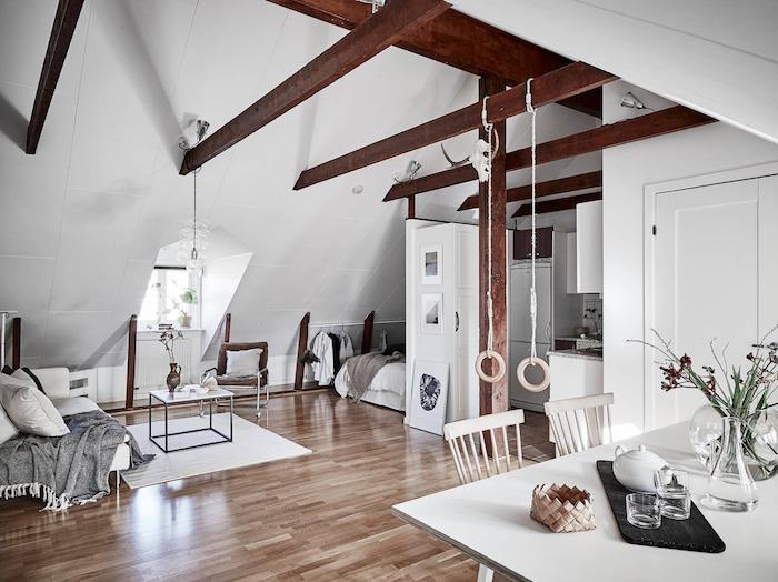 synliga balkar i en studio under sluttningen med sovplats under sluttningen, vit soffa med grå pläd, minimalistiskt bord, vit matsal i skandinavisk stil