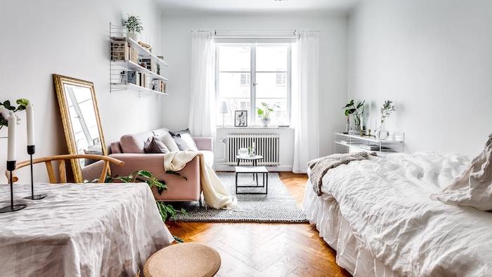 Nordisk inredning i ett designer sovrum med rosa soffa, vit säng, enkelbord, trägolv, bokhylla