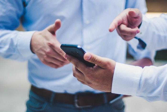 Två män i kostymer, händer som pekar på mobiltelefon, säkra betalningar