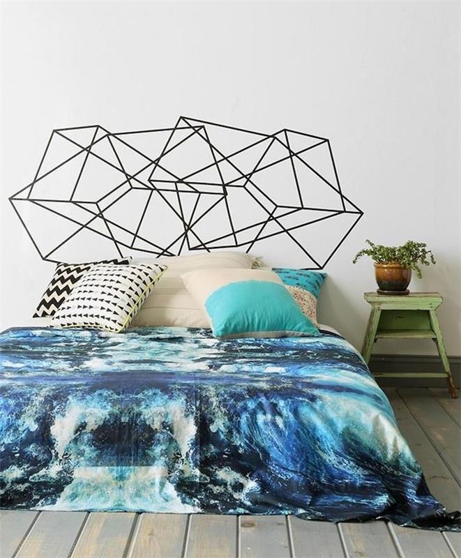 original sänggavel i svarta geometriska mönster, blå sänglinne, dekorativa kuddar, sliten grå parkett, vintage nattduksbord