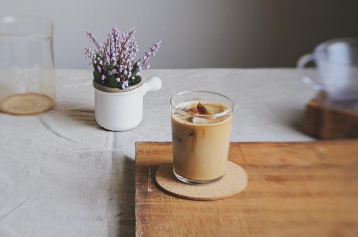recept na ľadovú kávu si môžete pripraviť sami, pohár studenej kávy s mliekom a kockami ľadu na drevenom podnose a pod sklom