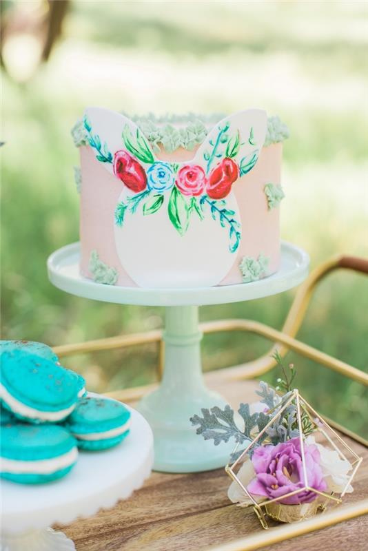 ganska lager tårta med slät rosa glasyr dekorerad med små blommor gjorda med en konditoriväska och ett papper kaninhuvud