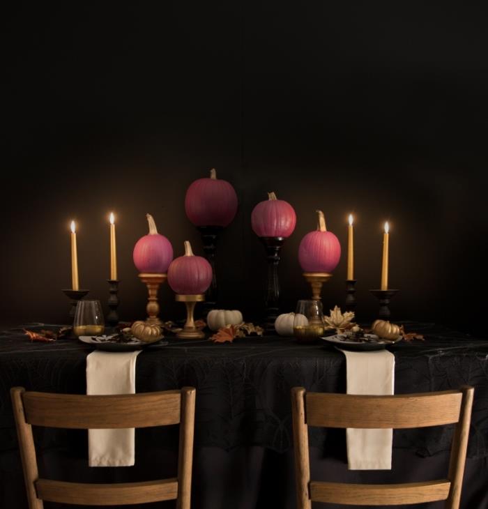 halloween bordsdekoration med svart duk och guldljusstakar, rosa målade pumpor på svart bord