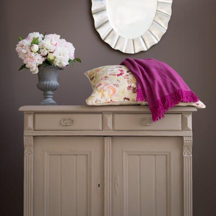 vynovený kus nábytku, komoda premaľovaná na sivú, purpurová deka a farebný vankúš s kvetinovou potlačou, kytica kvetov, tmavošedá stena, okrúhle zrkadlo