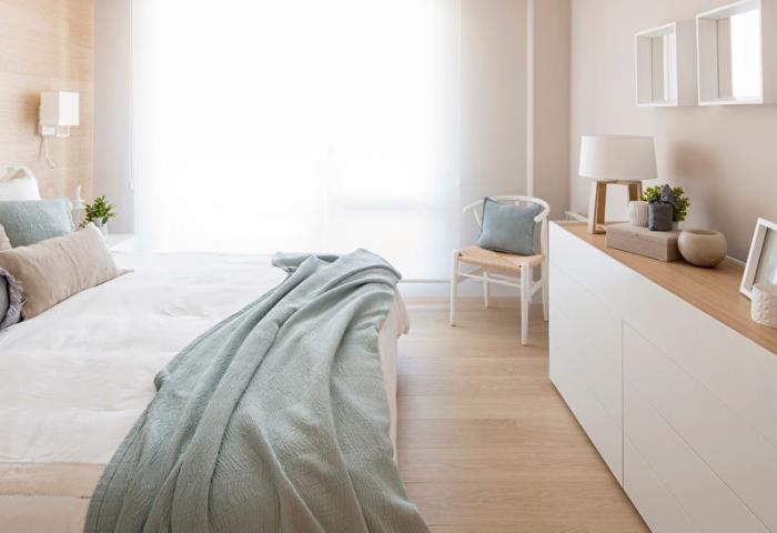 Skandinavisk och minimalistisk anda i sovrummet med ljusa träväggar och golv med pastellgröna kuddar och kast