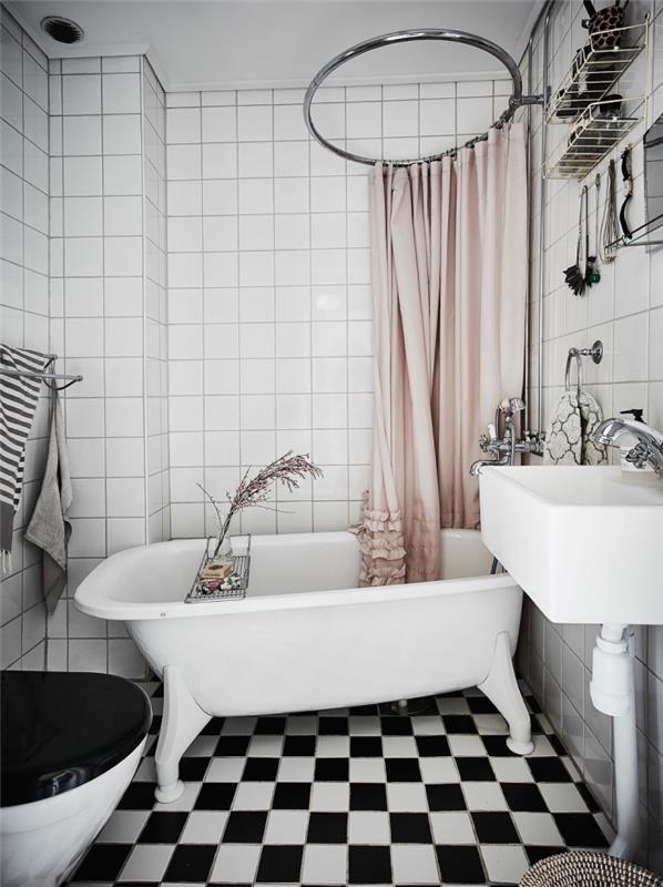mysig inredning i ett litet badrum i vitt och svart, liten fristående badkarsmodell, platsbesparande metallförvaring