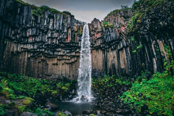 obrovská vodopádová fotografia so skalami a zelenými rastlinami na čiernych kameňoch, tapeta na pozadí s vodopádom